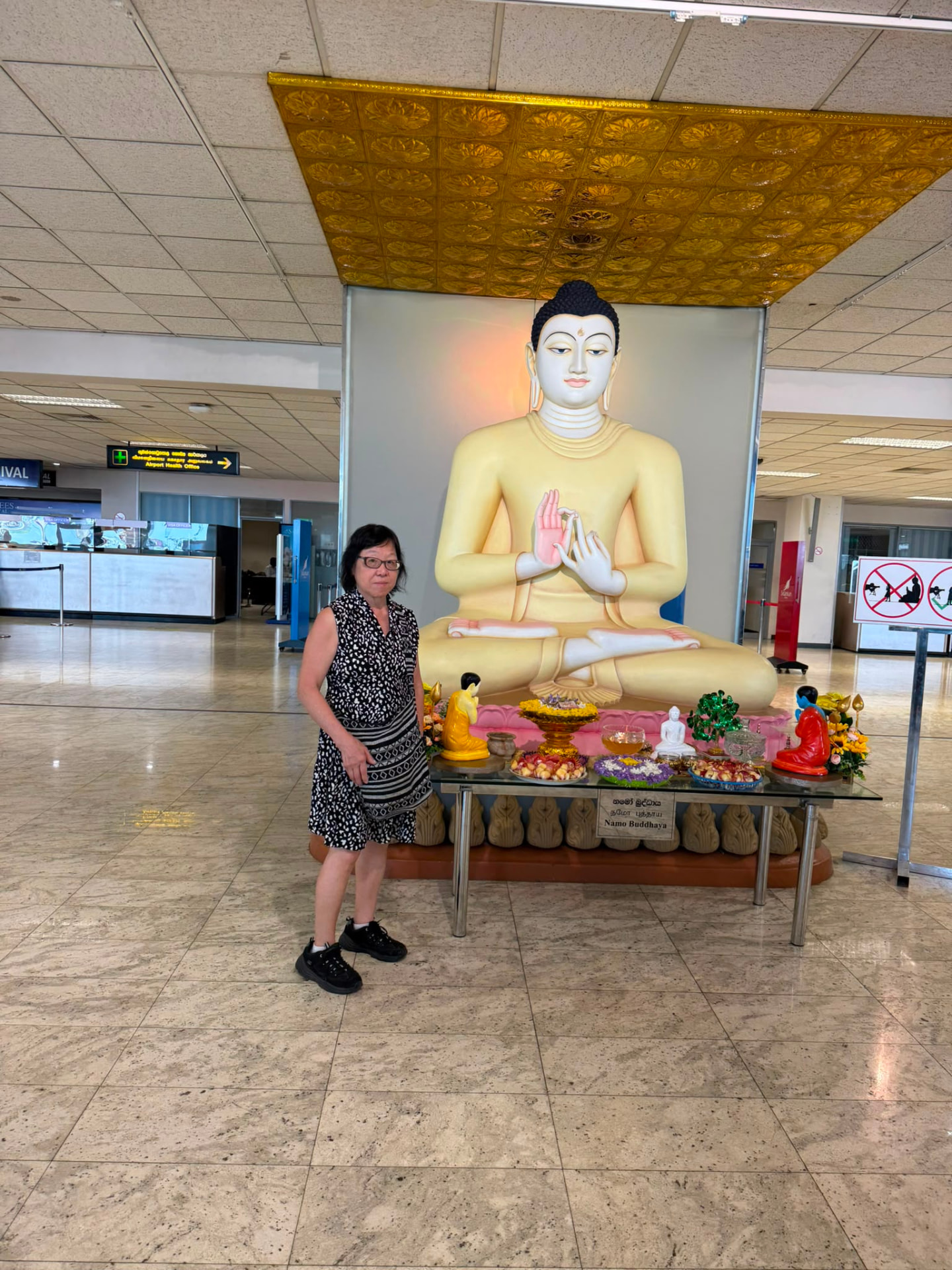 A traveller beside a golden Buddha statue and floral offerings on arrival in the Far East